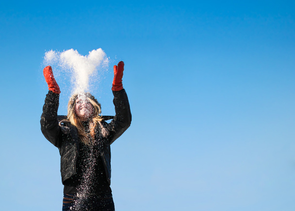 Happy girl with heart-shaped snow on sunny winter day against blue sky - Φωτογραφία, εικόνα