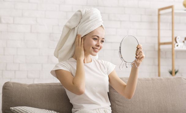 Woman looking at mirror, wearing towel on head after shower - Photo, Image