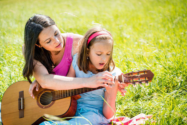 Mother teaches plaing guitar her child - outdoor in nature on sunny day - Foto, Imagen