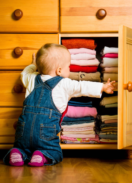 Baby throws out clothes from wooden furniture at home - Foto, immagini
