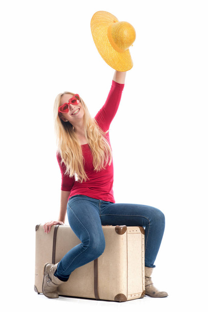 a woman sitting on a suitcase and waving with her summer hat - 写真・画像