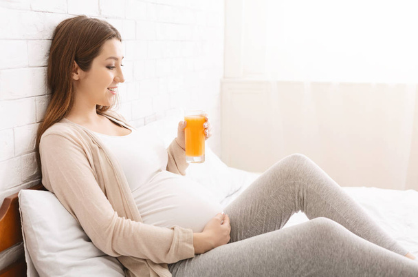 Pregnant woman enjoying glass with freshly made orange juice - Fotoğraf, Görsel