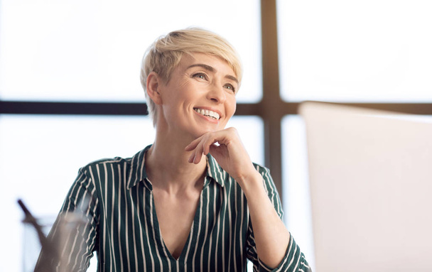 fröhliche Geschäftsfrau sitzt am Arbeitsplatz im Büro - Foto, Bild