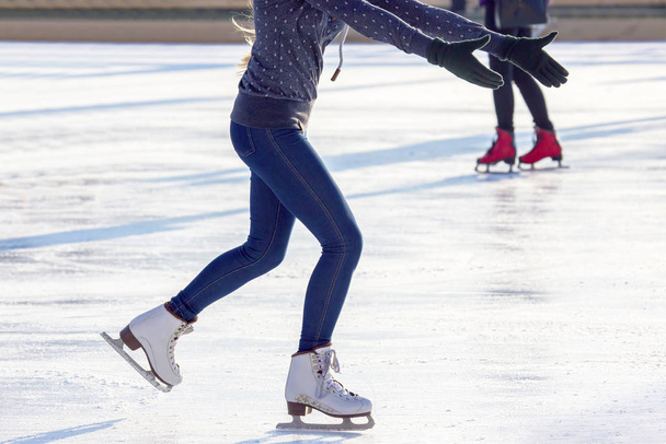 πόδια ενός κοριτσιού με μπλε τζιν και άσπρα πατίνια σε παγοδρόμιο. χύ - Φωτογραφία, εικόνα