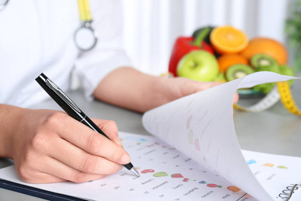 Female nutritionist with list of products at table, closeup - Фото, изображение