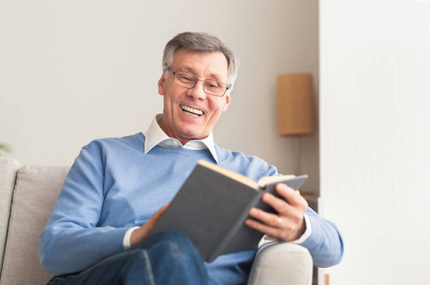 starší muž čtení knihy sedí na gauči doma - Fotografie, Obrázek