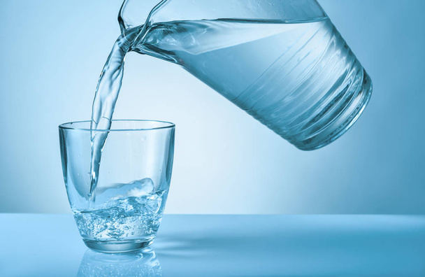 Pouring of fresh water into glass on color background - Photo, Image