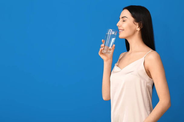 Hermosa joven con vaso de agua sobre fondo de color
 - Foto, Imagen