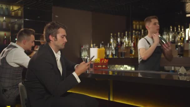 Muž sedí v telefonu u baru, barman třese alkoholem - Záběry, video