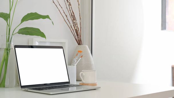 Περικοπή στιγμιότυπο του ελάχιστου χώρου εργασίας με κενό φορητό υπολογιστή οθόνη, φλιτζάνι καφέ και κεραμικά διακοσμητικά  - Φωτογραφία, εικόνα