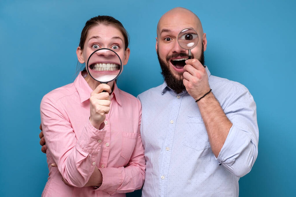 Cheerful pretty woman and man looking at camera through magnifying glass and zooming teeth - Foto, Imagen