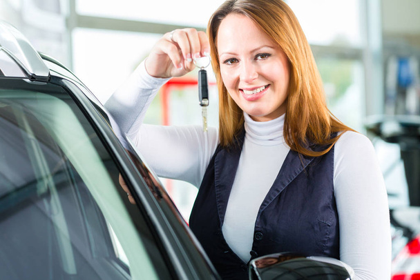 young woman stands next to car or new car in car dealership maybe she takes a test drive or she likes the car,she buys him and holds the keys - Foto, Bild
