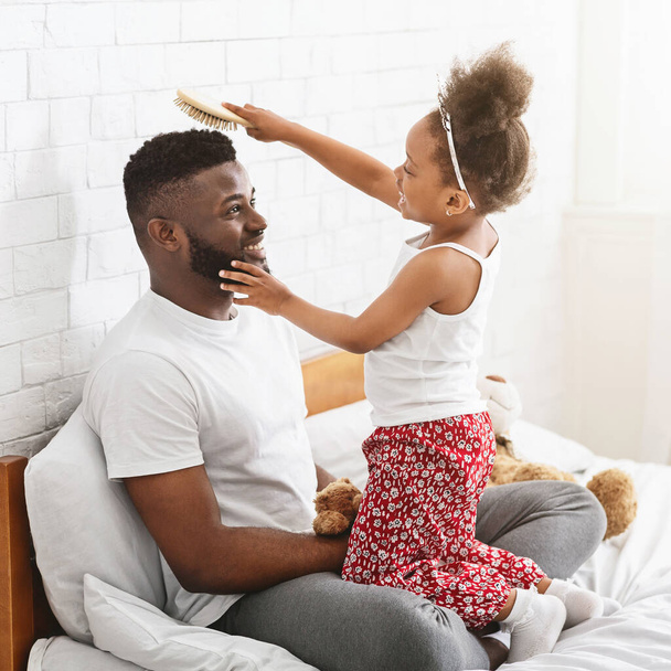Adorable chica negra en corona peinando el pelo de su padre
 - Foto, imagen