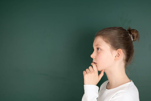 portrait of a thoughtful little girl in a green shirt and white t-school uniform on a black background - Valokuva, kuva
