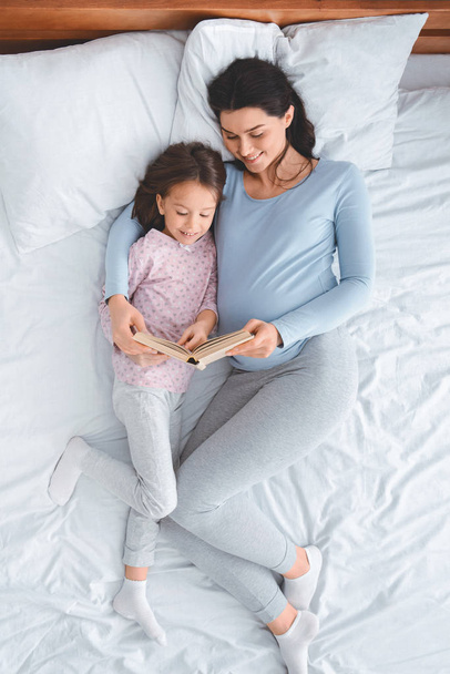 Top view of young expecting mom reading book to daughter - Photo, Image