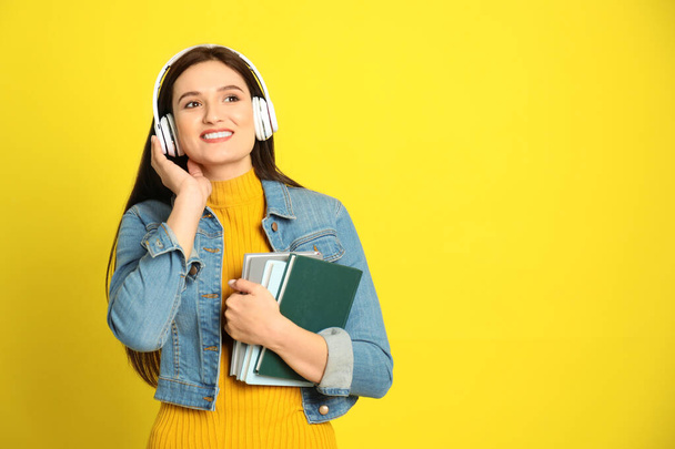 Young woman listening to audiobook on yellow background. Space for text - Фото, зображення