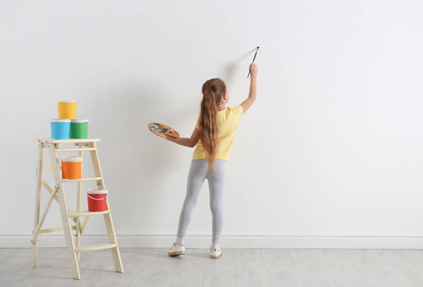 Little child painting on blank white wall indoors - Фото, изображение