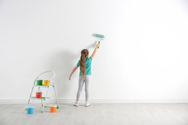 Little child painting with roller brush on white wall indoors. Space for text - Foto, Bild