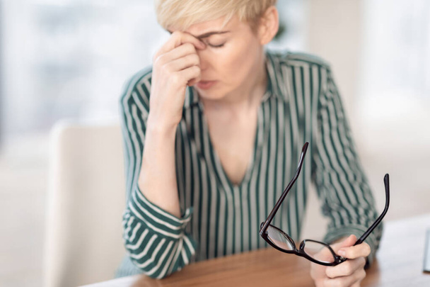 Dojrzałe bizneswoman posiadające Eyestrain ból głowy Masowanie Nosebridge w miejscu pracy - Zdjęcie, obraz