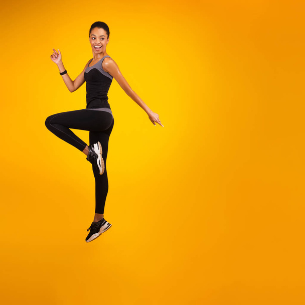 African American Lady Jumping Over Yellow Studio Background - Фото, изображение