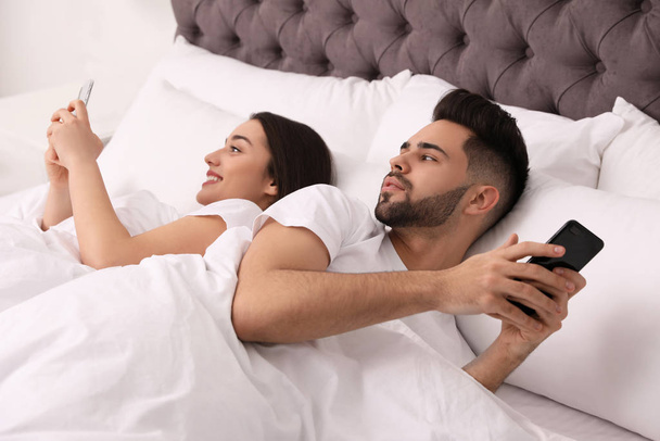 Young couple with smartphones in bed at home - Foto, Imagen