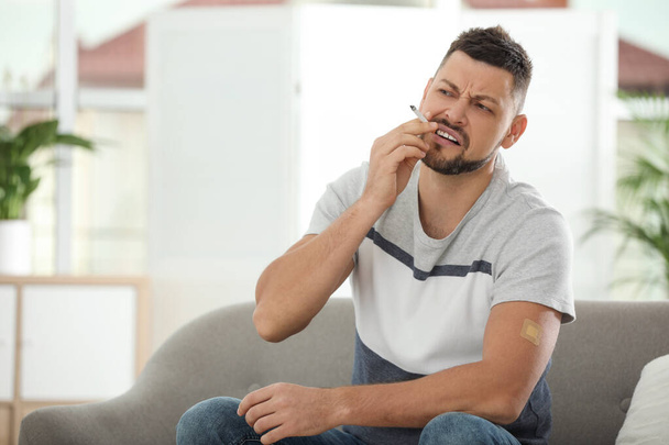 Emotional man with nicotine patch and cigarette at home - Photo, image
