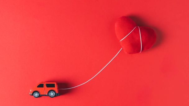 Kırmızı bir araba modeli kırmızı bir kalp yastığını çekiyor.  - Fotoğraf, Görsel
