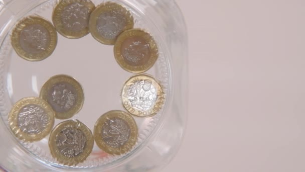 die Perspektive eines Wurms in Zeitlupe, der ein paar Pfund Münzen in ein Glas fallen lässt - Filmmaterial, Video