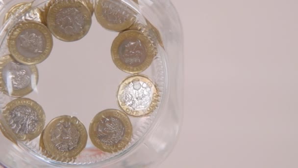 die Sicht eines Wurms in Zeitlupe auf jemanden, der ein paar Pfund Münzen in ein Glas fallen lässt - Filmmaterial, Video