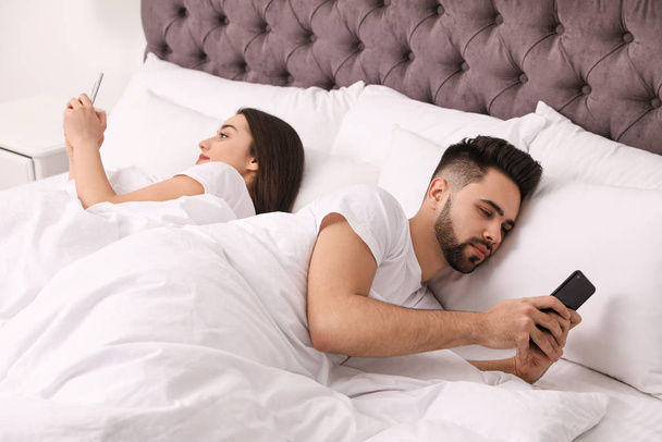 Young couple addicted to smartphones in bed at home - Fotoğraf, Görsel