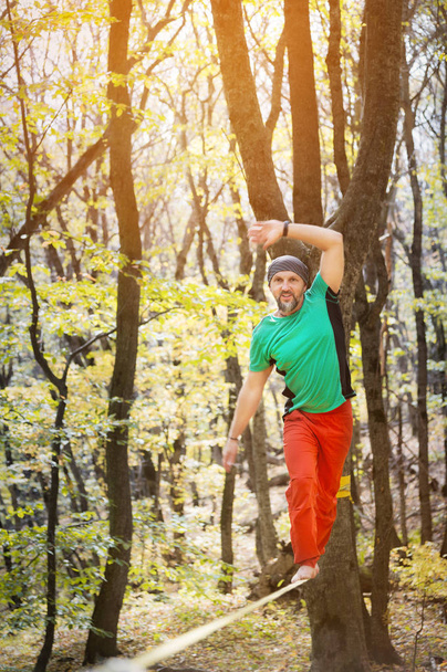 Male tightrope walker balancing barefoot on slackline in autumn forest. The concept of outdoor sports and active life of people aged - Valokuva, kuva