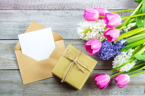 Mockup Anyák Napja koncepció. Tavaszi virágok tulipán és jácint, ajándék doboz és üres kártya kopott fa háttér. Üdvözlőlap nőknek vagy anyák napjára. Lapos fekvés, felülnézet, másolás. - Fotó, kép