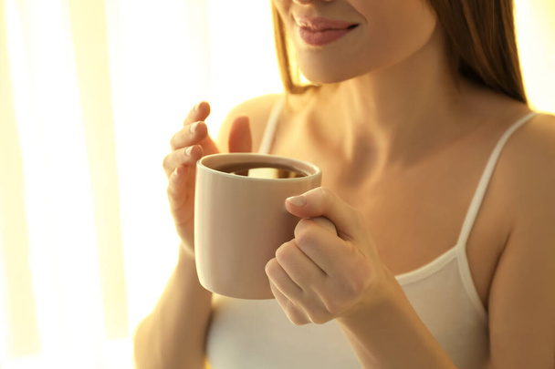 Young woman with cup near window at home, closeup. Lazy morning - Foto, Imagen