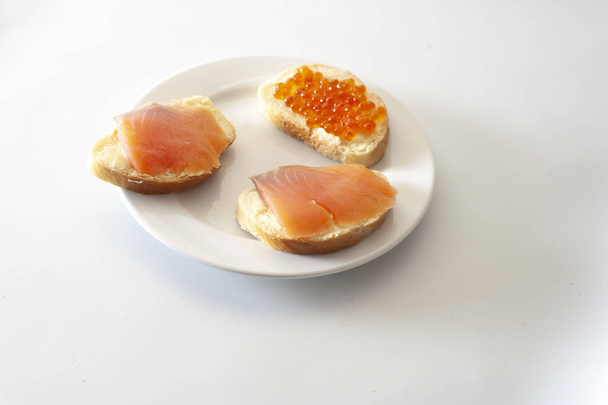 Tres pequeños sándwiches con caviar rojo y gallineta nórdica (salmón) en un plato blanco
. - Foto, imagen