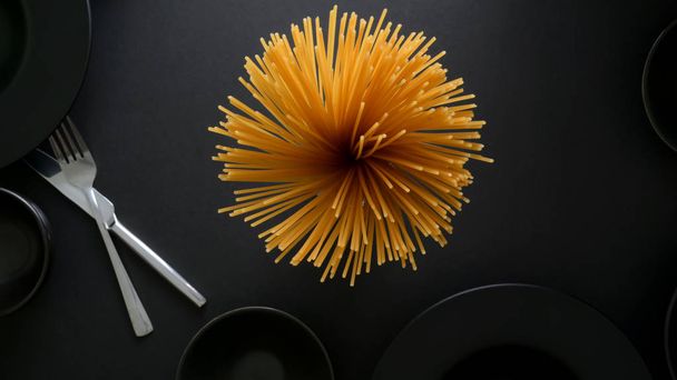 Nad głową ujęcie żółtego długiego spaghetti na czarnej talerzu i sztućcach  - Zdjęcie, obraz