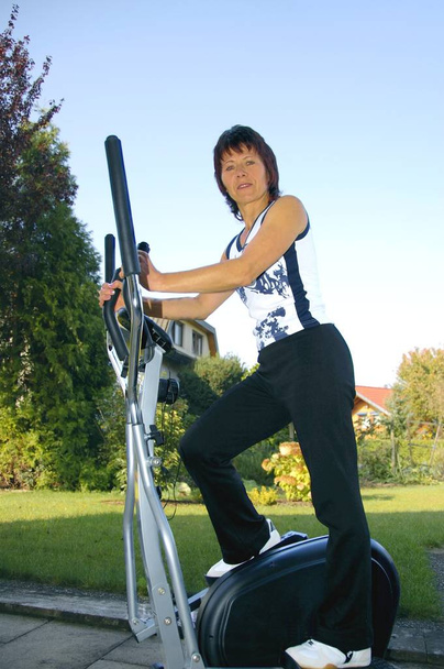 woman rolls on the home trainer in the garden of her home - Foto, Imagem