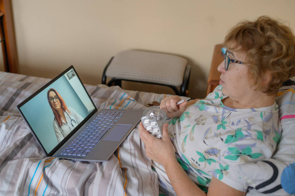 Egy idős nő beszél egy orvossal Skype-on. Egy nyugdíjas légúti betegségben szenved, és kifújja az orrát. Online konzultáció. - Fotó, kép