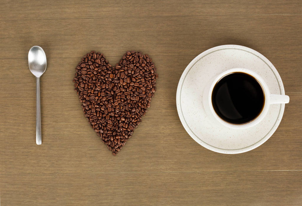 I love coffee. Heart shape made from coffee beans with a spoon and cup of coffee on hessian spelling - Photo, Image