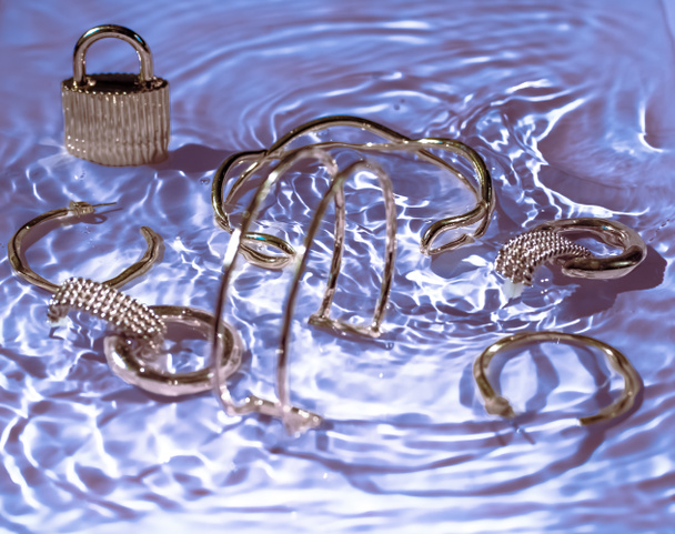 Pulseras de oro, pendientes, anillos, joyas en agua púrpura espalda
 - Foto, imagen