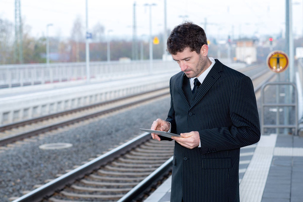 businessman on railroad station is waiting and using tablet pc - Φωτογραφία, εικόνα