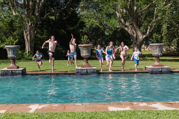 Girls boys teenagers young running jumping into home  swimming pool summer playtime - Fotó, kép