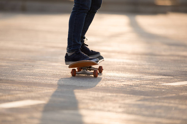 Legs of skateboarder riding board at sunrise on city road  - Foto, afbeelding