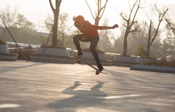 Female skateboarder skateboarding at sunrise in urban park - Foto, Bild