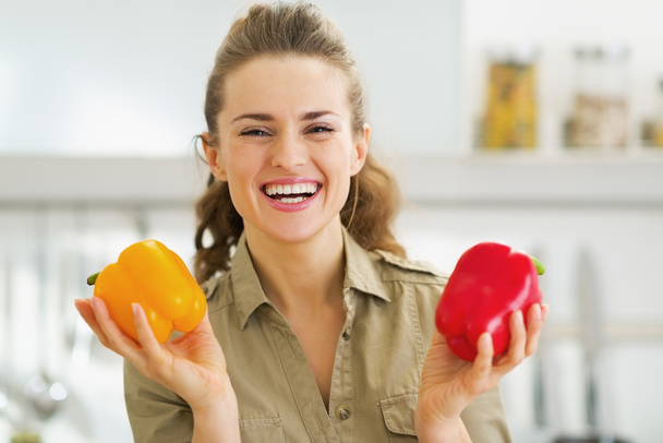 Happy young housewife holding red and yellow bell peppers - Foto, Imagen