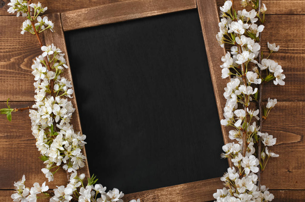 Old blank vintage school slate or chalkboard lying on an old rustic wooden background with dainty white flowers in two corners ready for your text or message - Foto, imagen