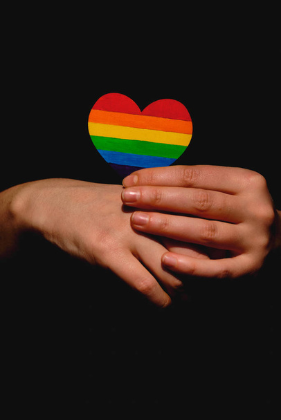 Női karok tartják a szívet színes Lgbt büszkeség színek a sötét háttérben. A homofóbia, a szexuális egyenlőség, a feminizmus és a szociális biztonság elleni világnap koncepciója - Fotó, kép