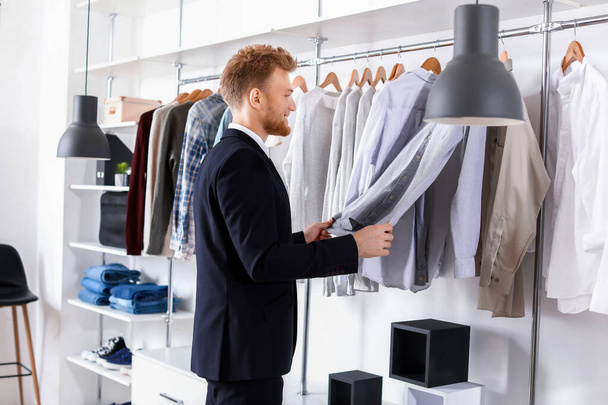 Handsome man choosing clothes in dressing room - Photo, Image