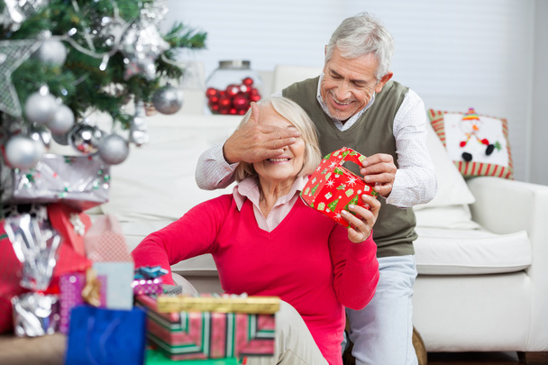 Hombre feliz cubriendo los ojos de la mujer mientras da regalo de Navidad
 - Foto, imagen