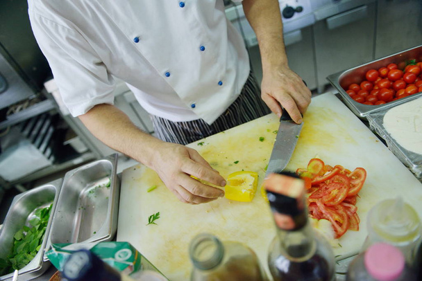 Handsome chef dressed in white uniform decorating pasta salad and seafood fish in modern kitchen - Foto, Imagem