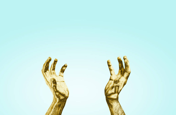 Manos doradas levantadas sobre un fondo azul pastel. El concepto de predicar ideas, levantar las manos para atrapar algo. Las manos de color dorado alcanzan el cielo
. - Foto, Imagen